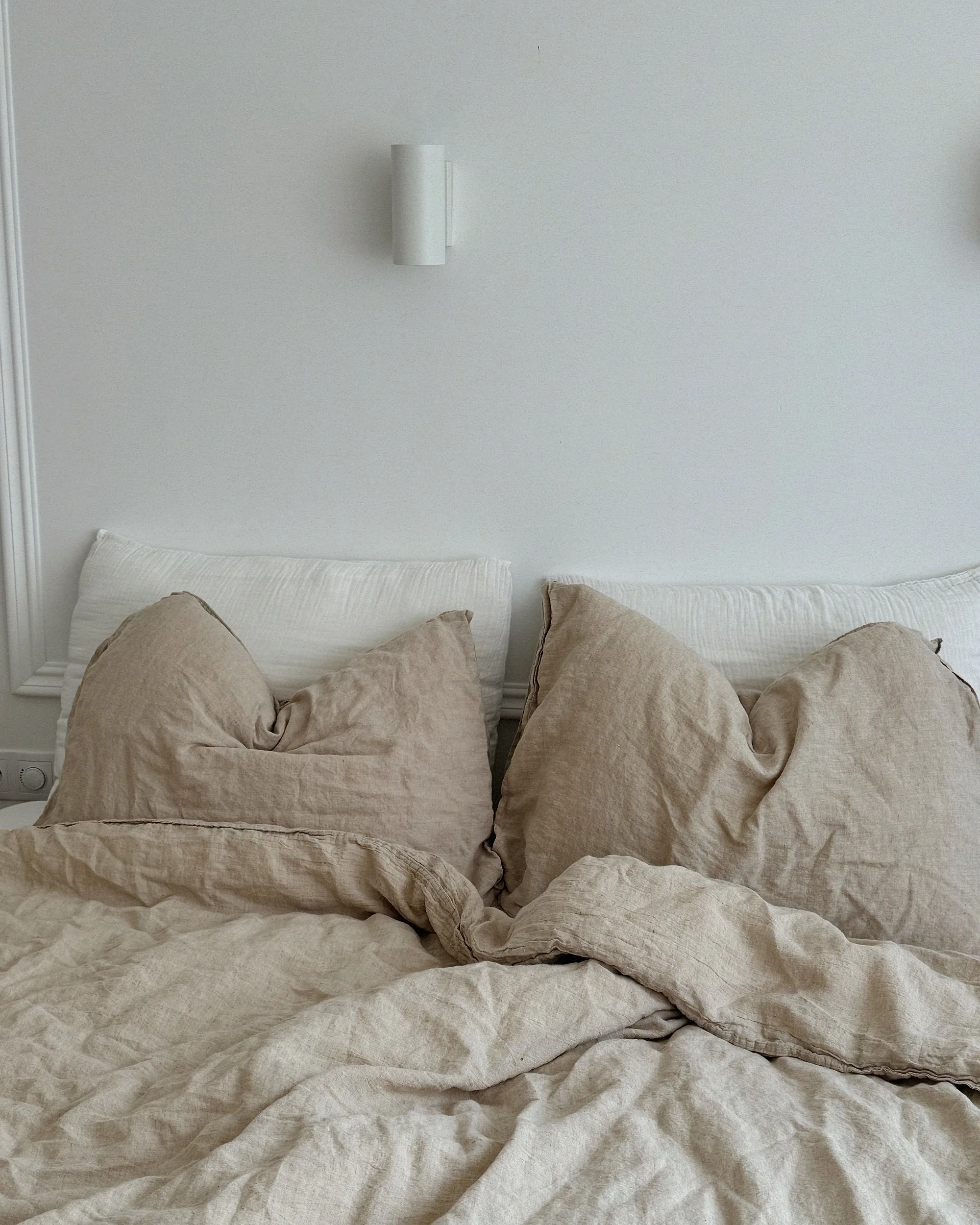 Letto sfatto con biancheria di lino color sabbia